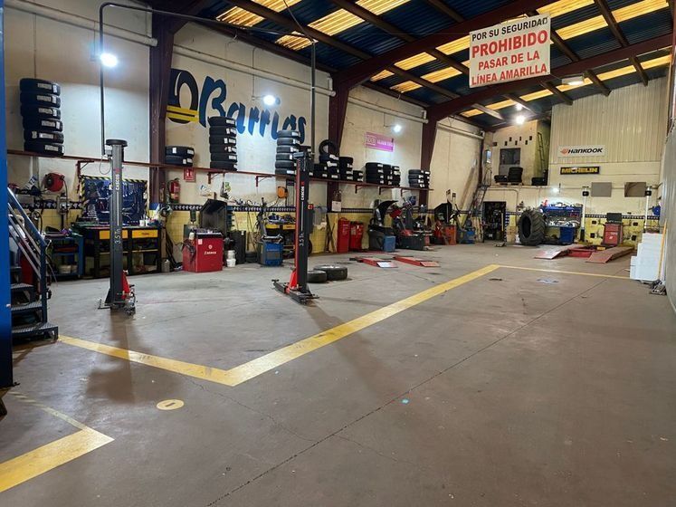 Interior de un taller mecánico con herramientas, portaneumáticos y elevador. Líneas amarillas en el suelo e iluminación cenital.