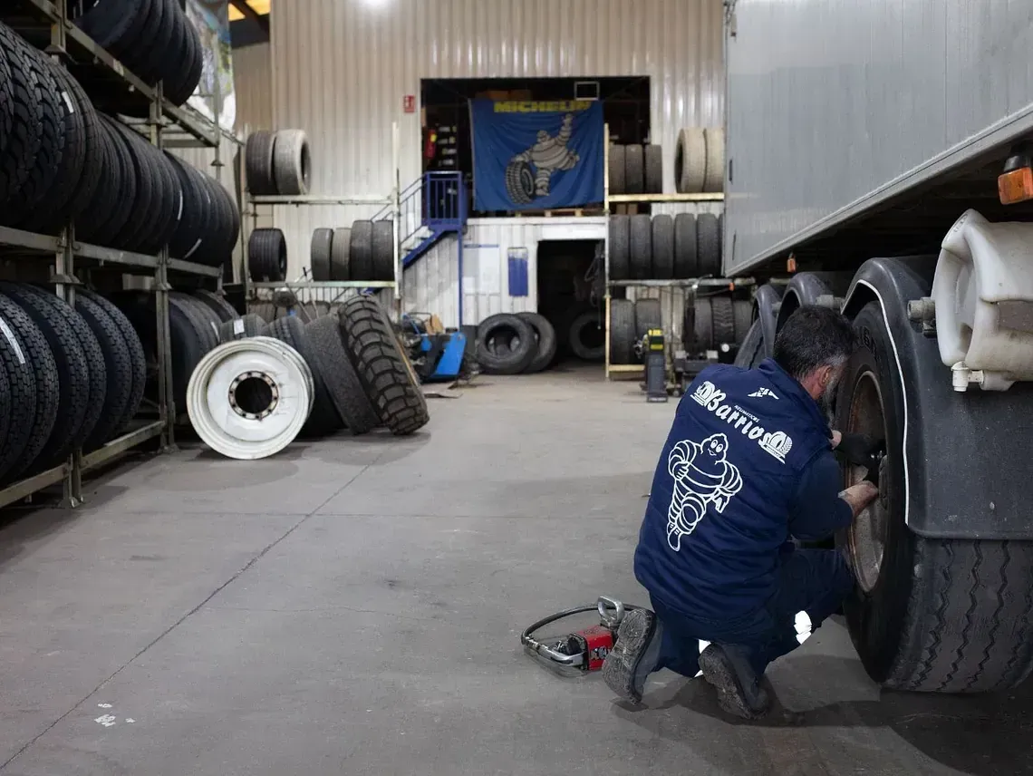 Mecánico trabajando en un neumático de camión en un taller de neumáticos, rodeado de neumáticos en los estantes.