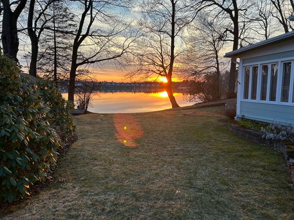 The sun is setting over a lake with a house in the foreground.