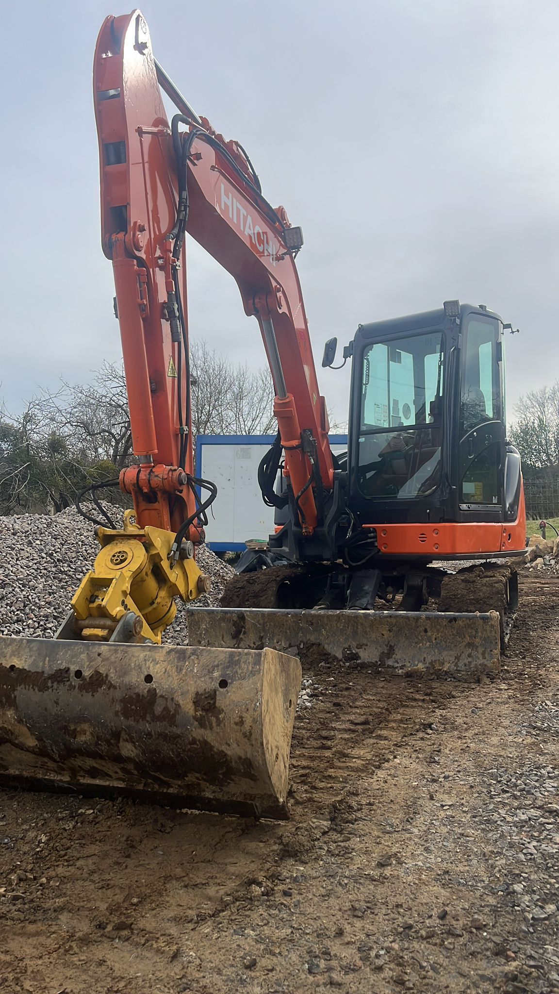 Excavadoras amarillas y un camión volquete trabajan en una obra de construcción en un paisaje rural y montañoso.