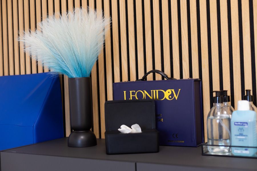 Blaue Vase, schwarze Box und LEONIDEX-Display mit Flaschen auf einem gestreiften Regalhintergrund