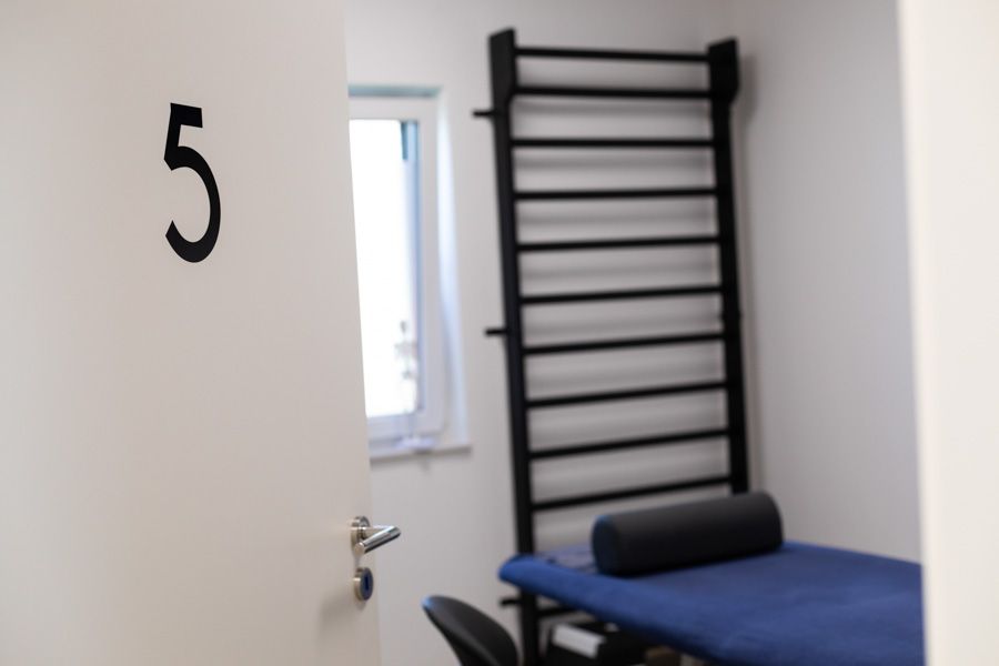 Nummer 5 an einer Wand neben einem kleinen Untersuchungsraum mit Fenster, Gitterstäben und einer blauen Behandlungsliege.