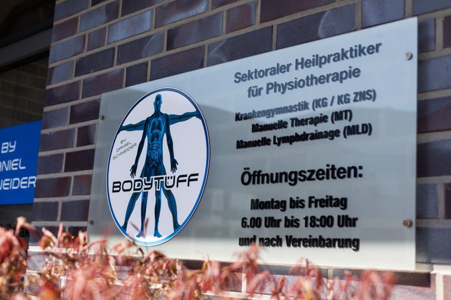 Schild der Physiotherapiepraxis Bodystuff in deutscher Sprache, weiß mit blauem Logo und Öffnungszeiten.