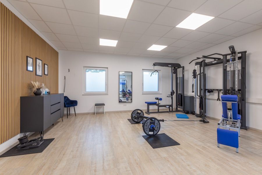 Moderner Fitnessraum mit Trainingsgeräten, Hanteln und hellem Holzboden