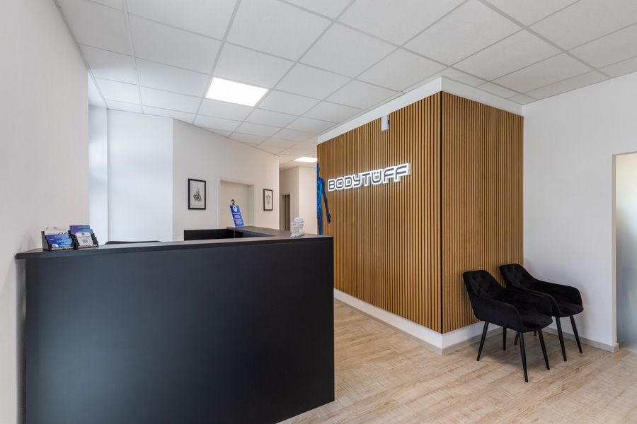 Moderner Empfangsbereich einer Klinik mit schwarzem Schreibtisch, Akzentwand aus Holz und angrenzendem Flur