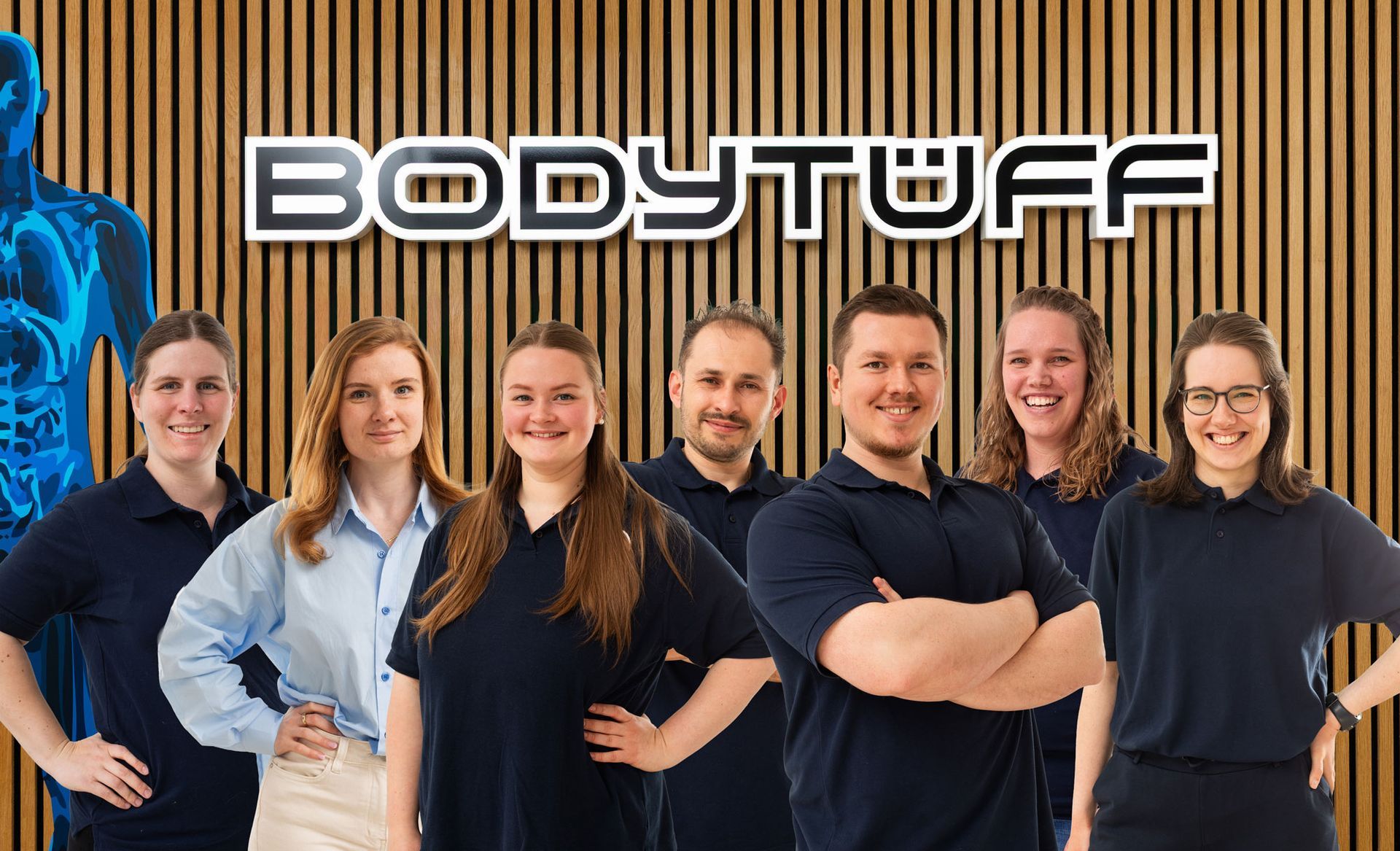 Sieben Personen posieren vor einem Bodystuff-Schild; sie tragen schwarze und hellblaue Hemden.