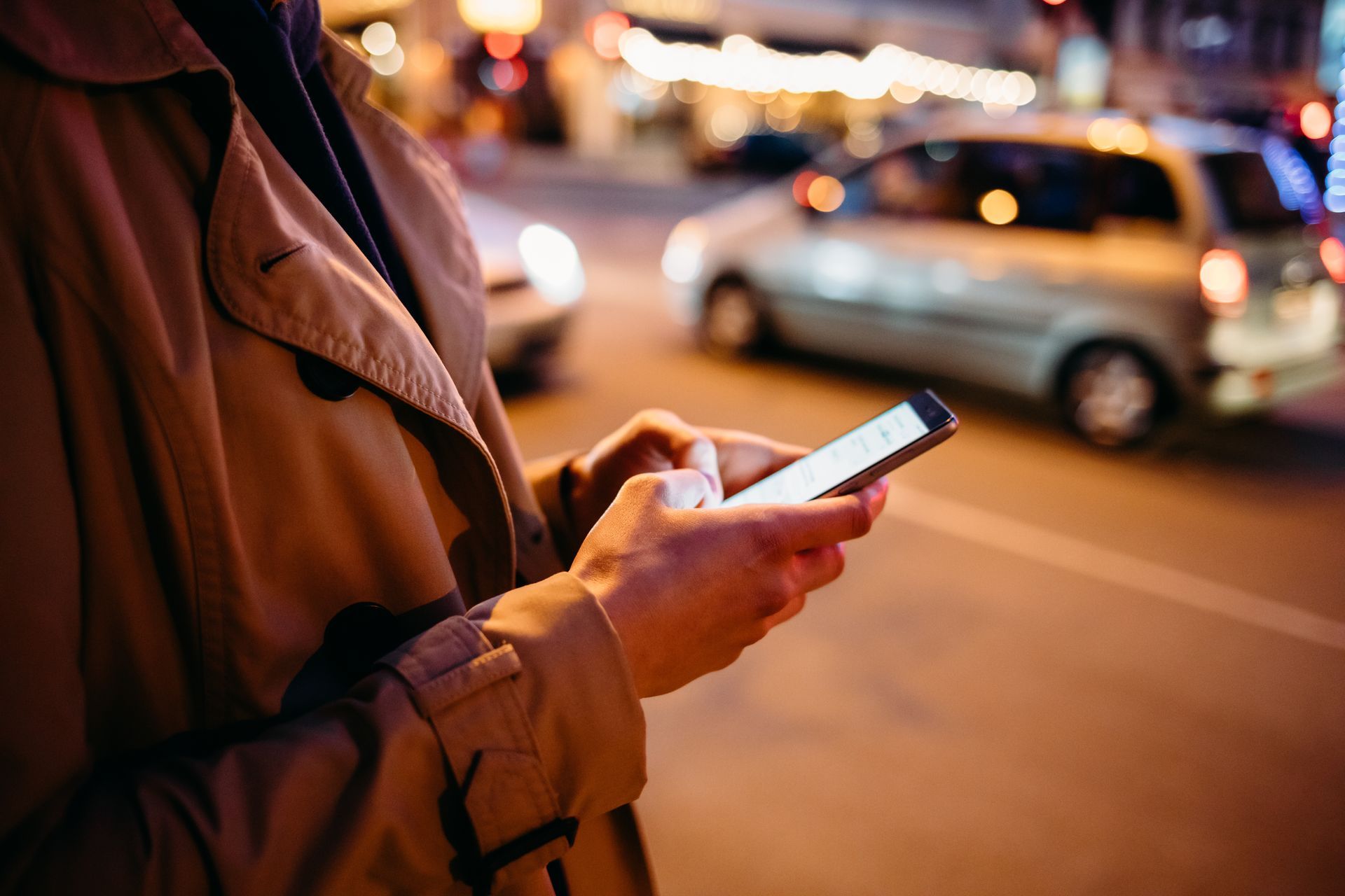 Eine Person benutzt nachts auf einer Stadtstraße ein Mobiltelefon.