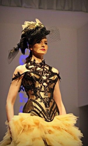 Modelo de pasarela con top de encaje negro, falda amarilla de tul y un llamativo tocado de plumas