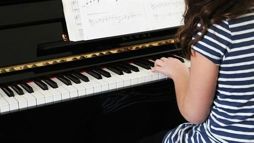 Ein junges Mädchen in einem gestreiften Hemd spielt Klavier.