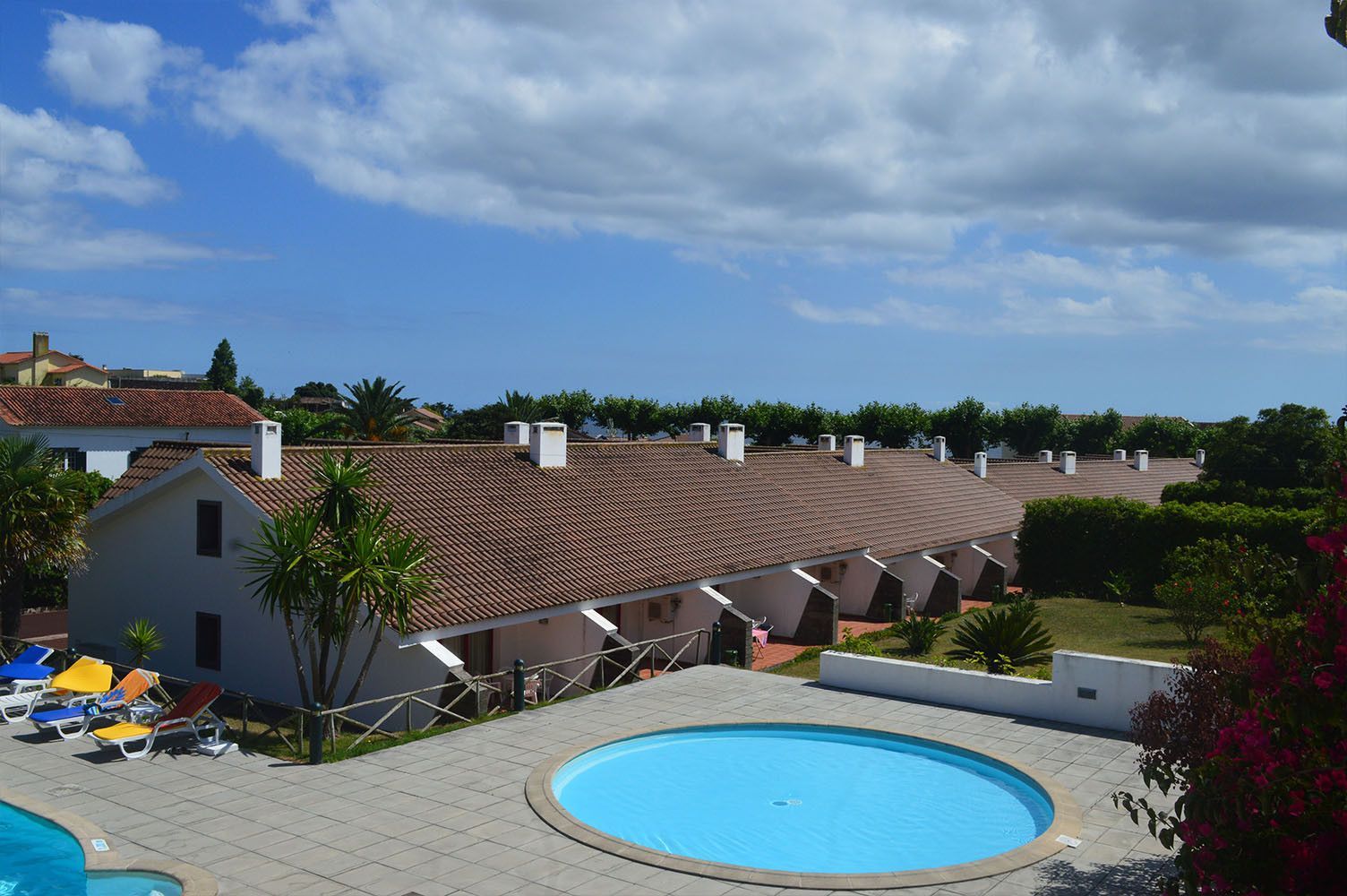 Fileira de casas brancas com telhados de telha vermelha, piscina, céu azul.