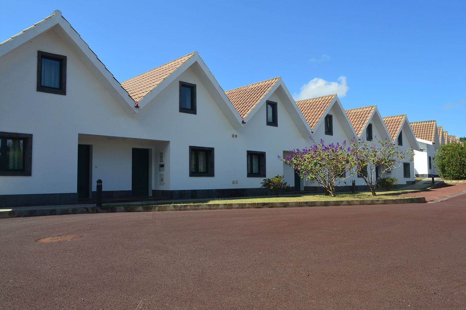 Fileira de prédios brancos com telhados pontiagudos e telhas marrons, sobre uma superfície marrom-avermelhada