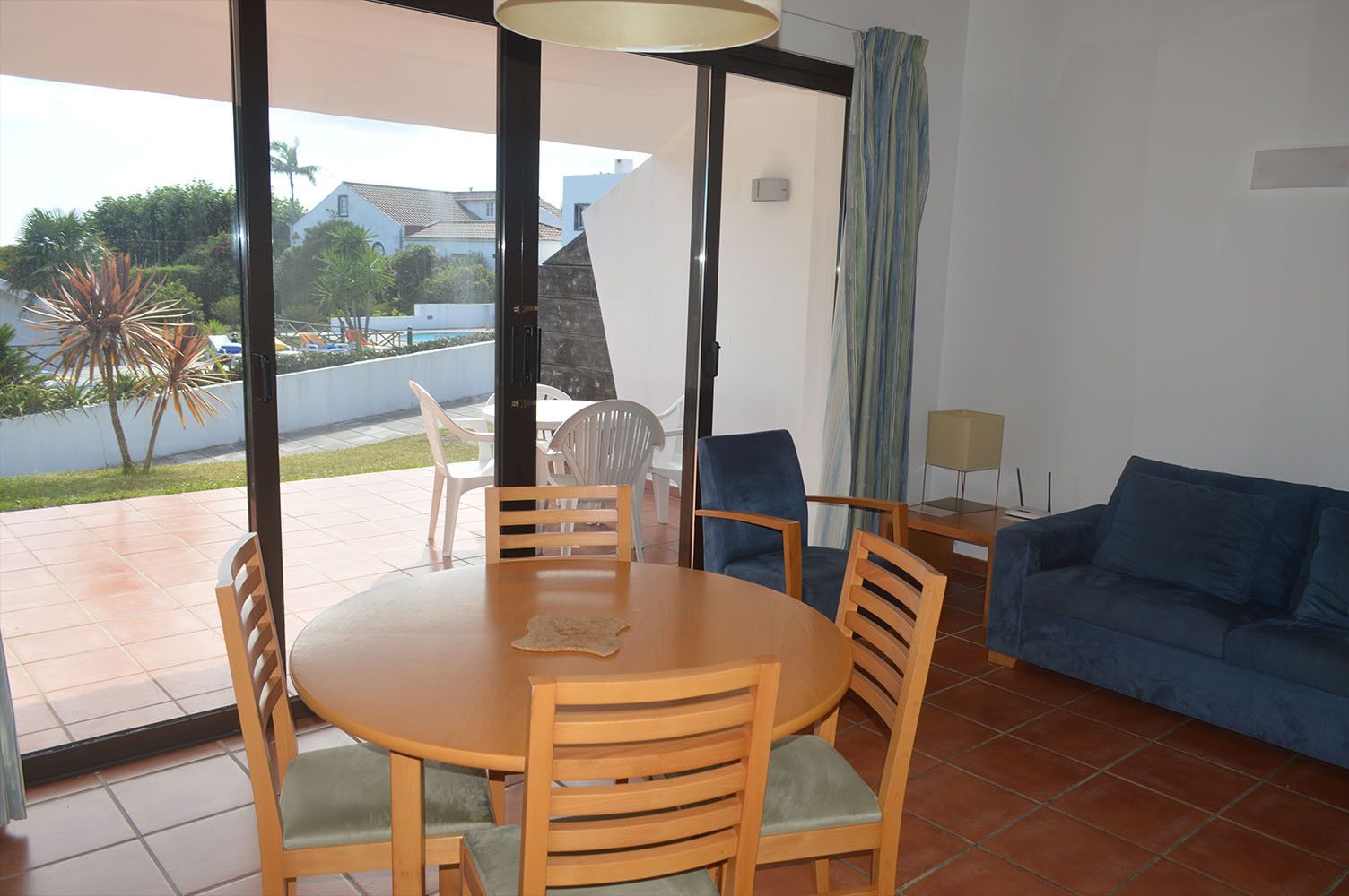 Sala de jantar com mesa redonda de madeira e cadeiras, porta de vidro deslizante para o quintal.