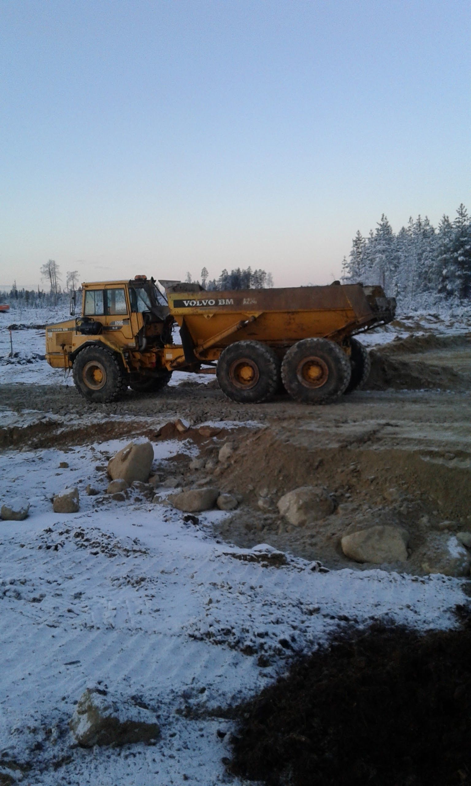 Keltainen nivelkippiauto lumisella rakennustyömaalla.