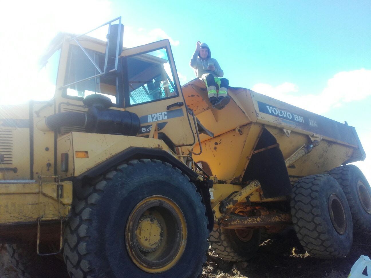 Keltainen Volvo dumpperi, jonka päällä on ihminen, sininen taivas.
