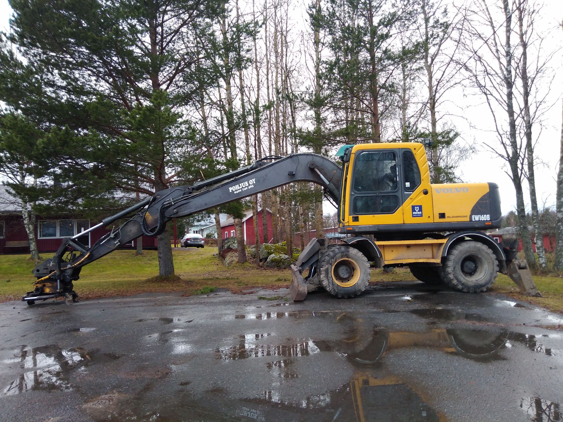 Keltainen Volvo-kaivinkone raivaa roskia asfalttitieltä maaseudulla.