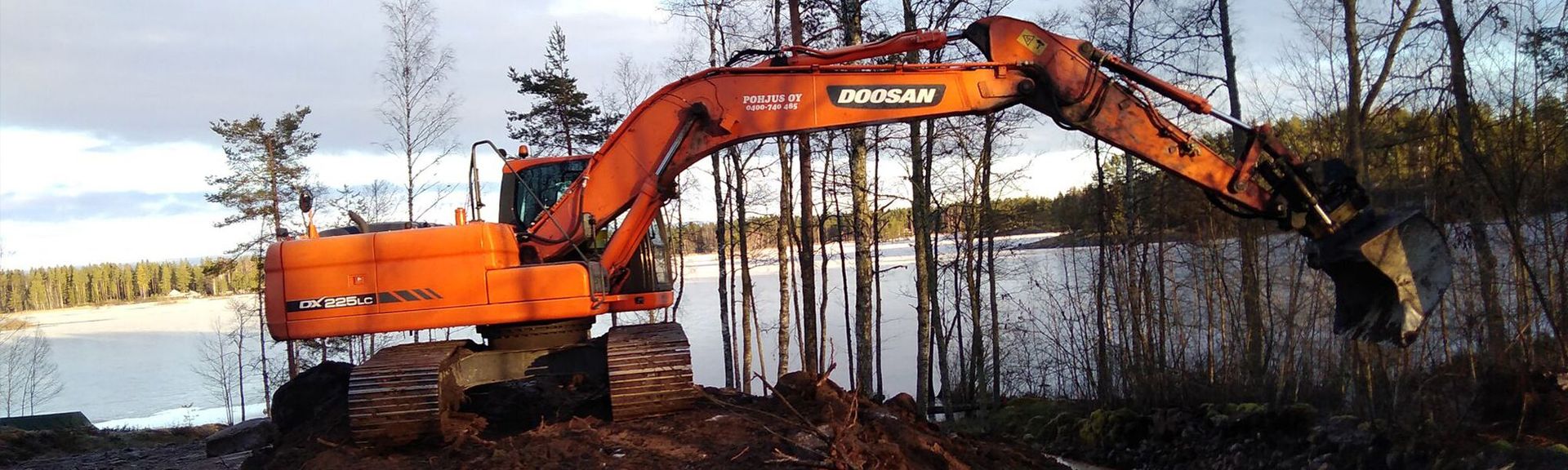 Oranssi kaivinkone järven rannalla.