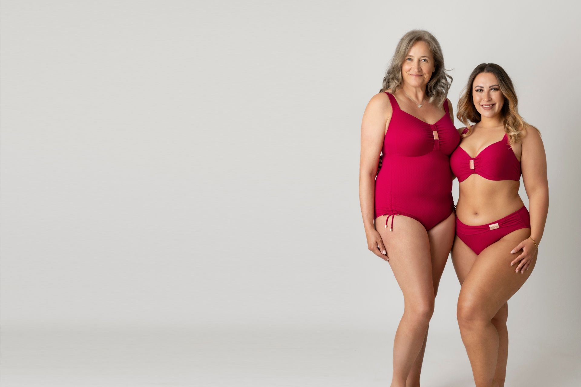 Zwei Frauen in roter Lingerie posieren vor einem weißen Hintergrund.