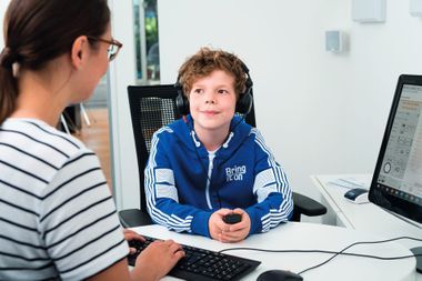 Junge mit Kopfhörern auf den Ohren sitzt bei der Hörgeräteakustikerin