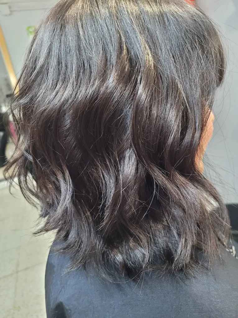 Cabello oscuro y ondulado hasta los hombros; la luz se refleja en los mechones, en un entorno de salón.