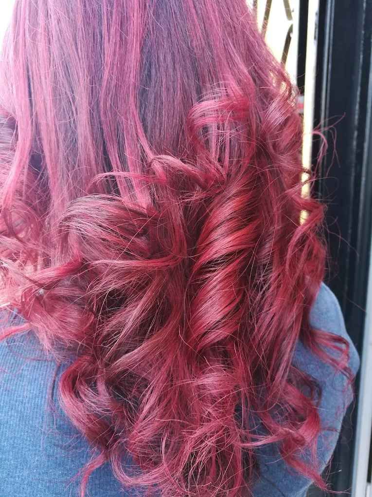 Cabello ondulado de color carmesí, que oculta parcialmente a una persona que viste una camisa azul.