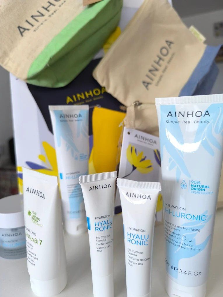 Una colección de productos de cuidado de la piel AINHOA en envases blancos y azules y bolsas de mano.