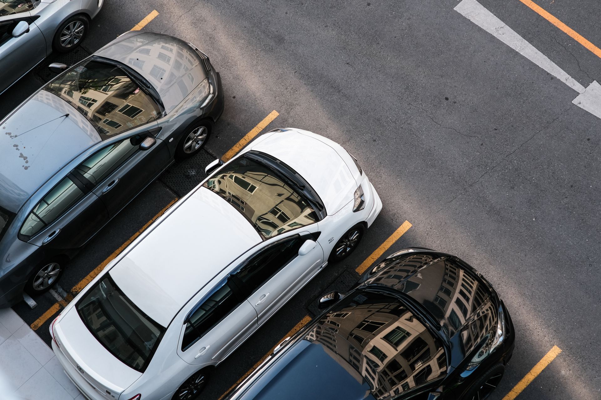 Vue en plongée de plusieurs voitures garées sur des emplacements délimités, sur un parking.