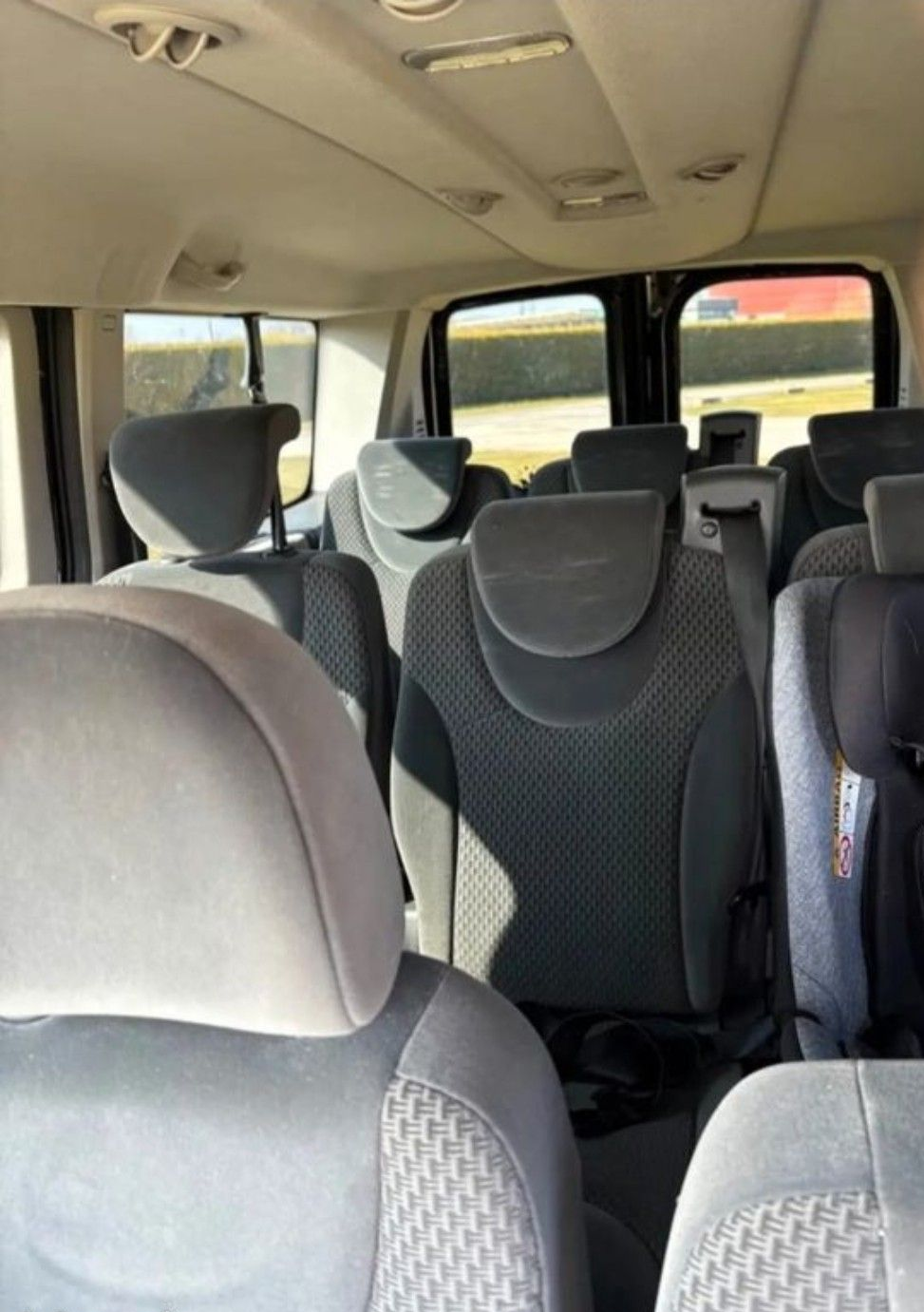 L'intérieur d'une camionnette montre plusieurs rangées de sièges en tissu gris, dont un siège auto pour enfant sur la rangée arrière.