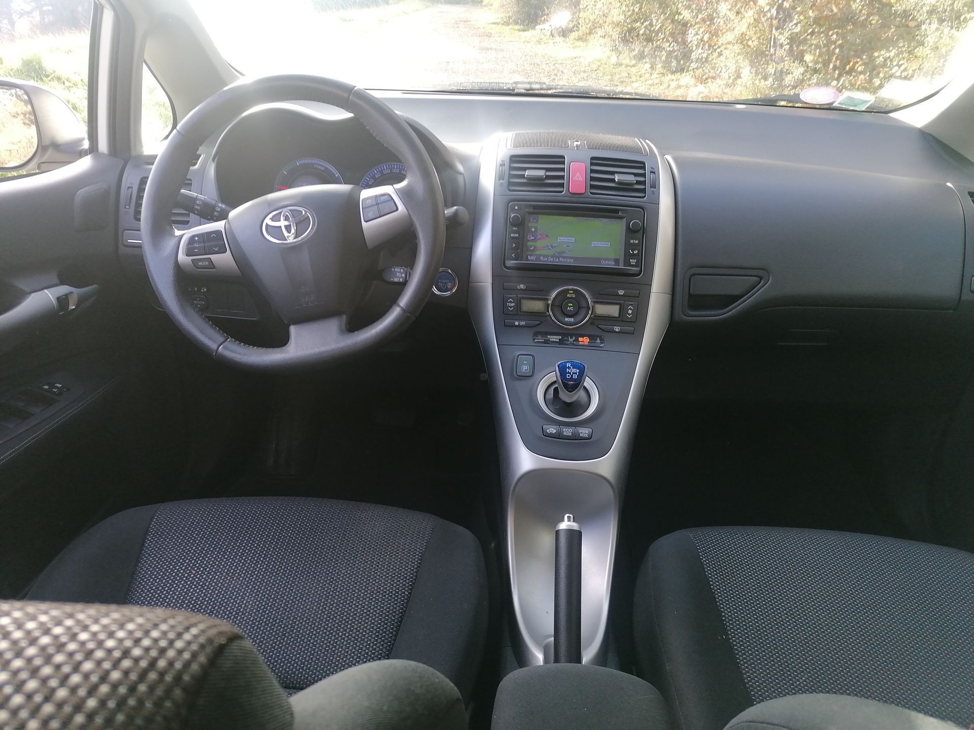 L'intérieur d'un véhicule Toyota montrant un volant, un tableau de bord, une console centrale et des sièges en tissu à motifs.