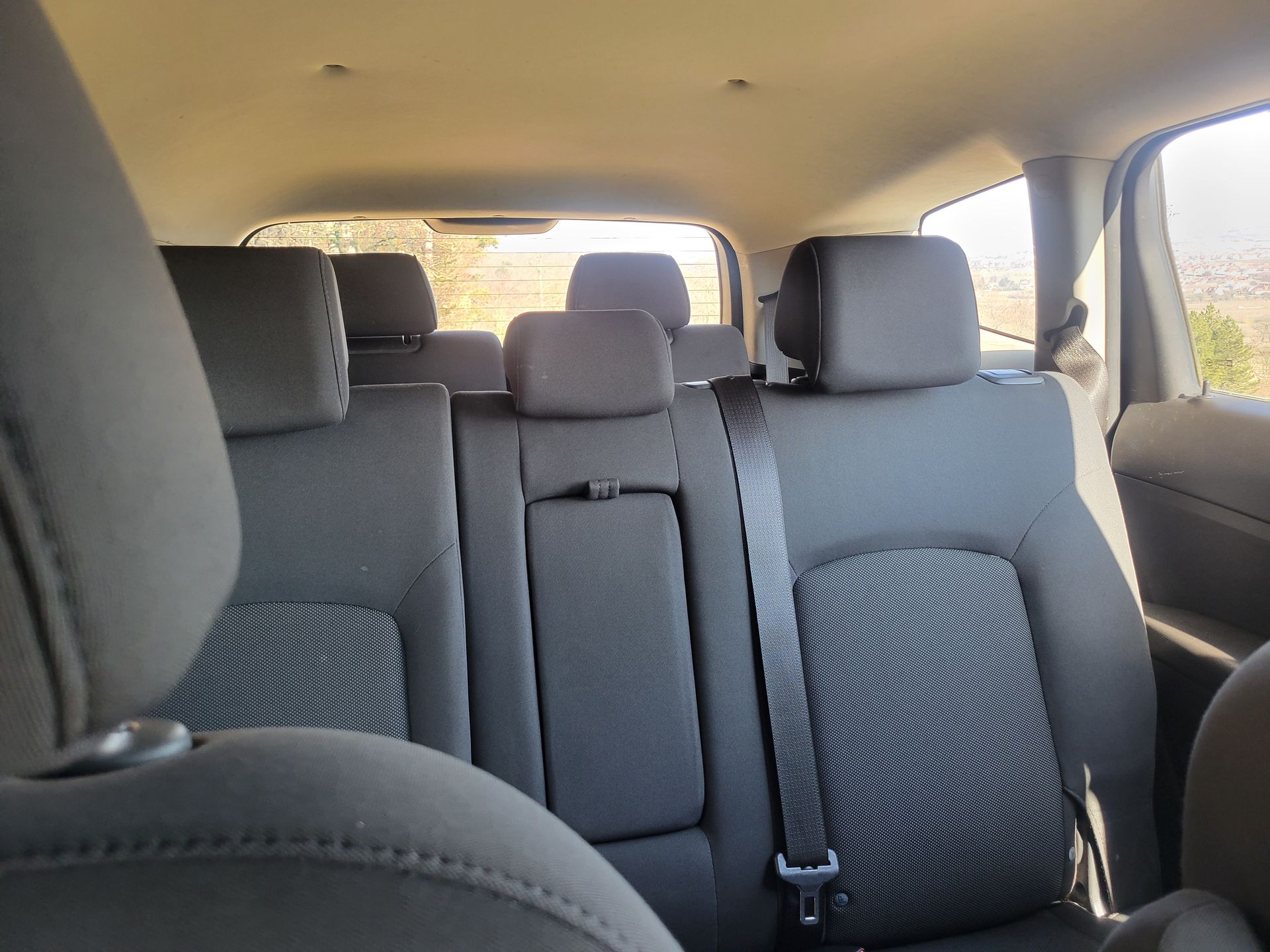 Banquette arrière d'un véhicule avec sellerie en tissu gris foncé, trois appuie-tête réglables et ceintures de sécurité.