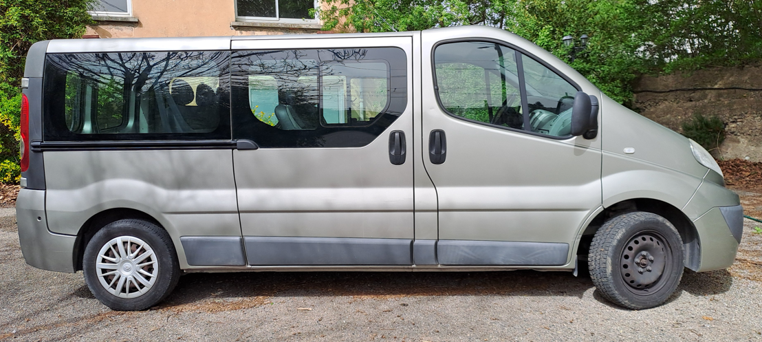 Vue latérale d'une fourgonnette argentée garée sur une surface gravillonnée à l'extérieur.