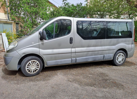 Une camionnette grise de transport de passagers garée à l'extérieur sur une surface gravillonnée.
