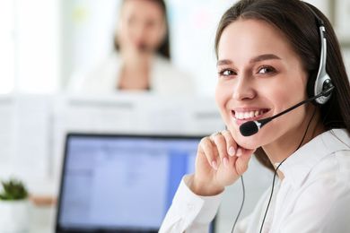 Eine Frau mit Headset lächelt, während sie vor einem Laptop sitzt.