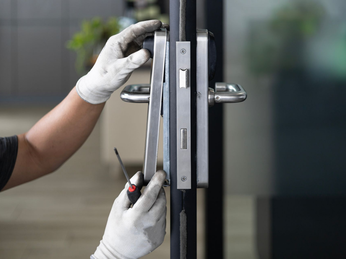 Des mains gantées utilisent un tournevis pour ajuster le mécanisme de verrouillage d'une porte métallique