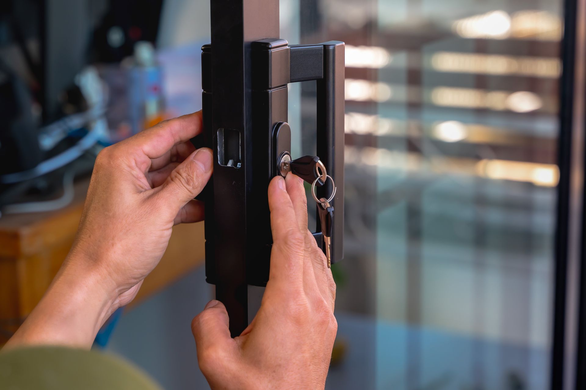 Des mains ouvrant une poignée de fenêtre noire sur une porte ou une fenêtre en verre.