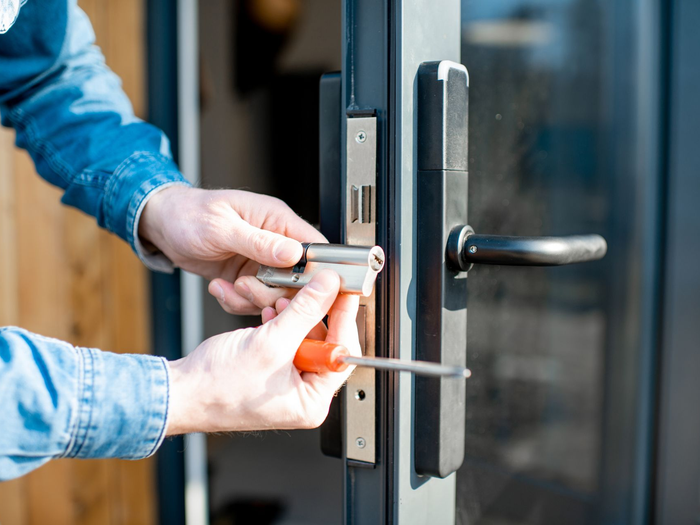 Des mains insérant une clé dans une serrure de porte argentée sur une poignée noire