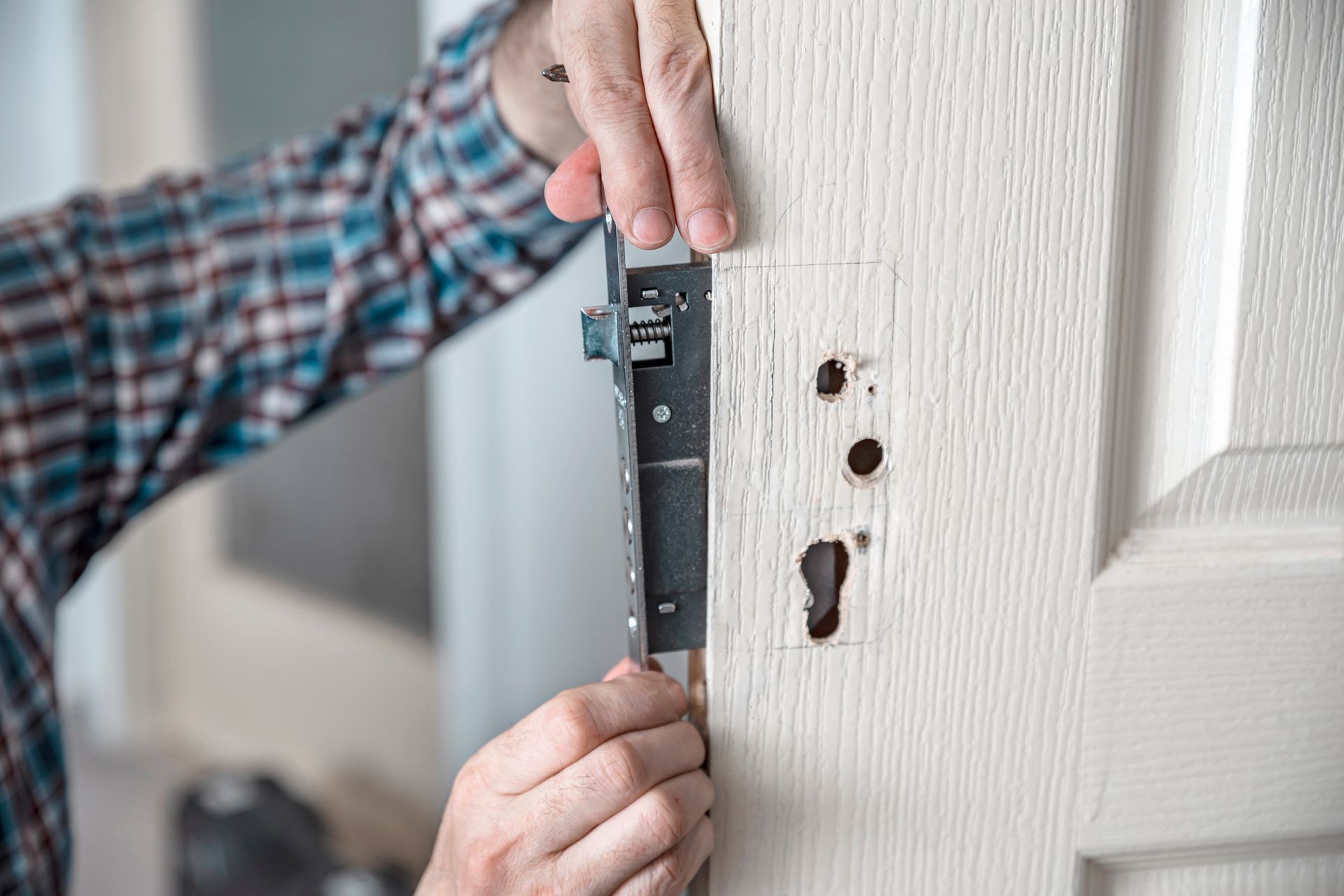 Des mains mesurent une serrure de porte avec une règle sur un cadre de porte blanc.