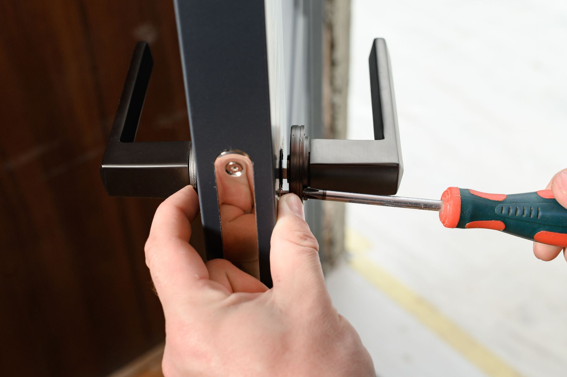 Des mains utilisent un tournevis pour serrer une poignée de porte noire sur une porte vitrée