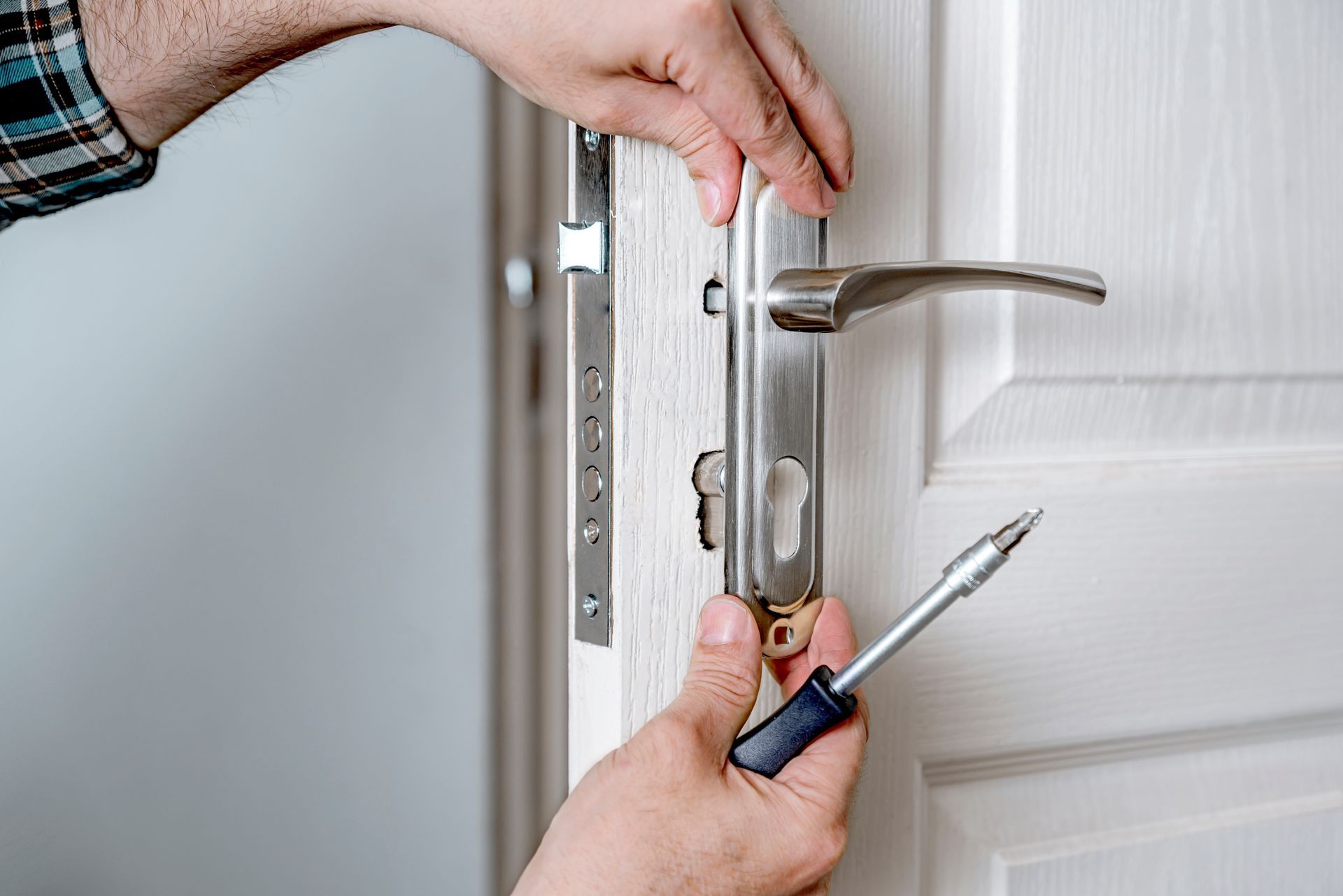 Des mains manipulent une serrure de porte blanche à l'aide d'un tournevis.