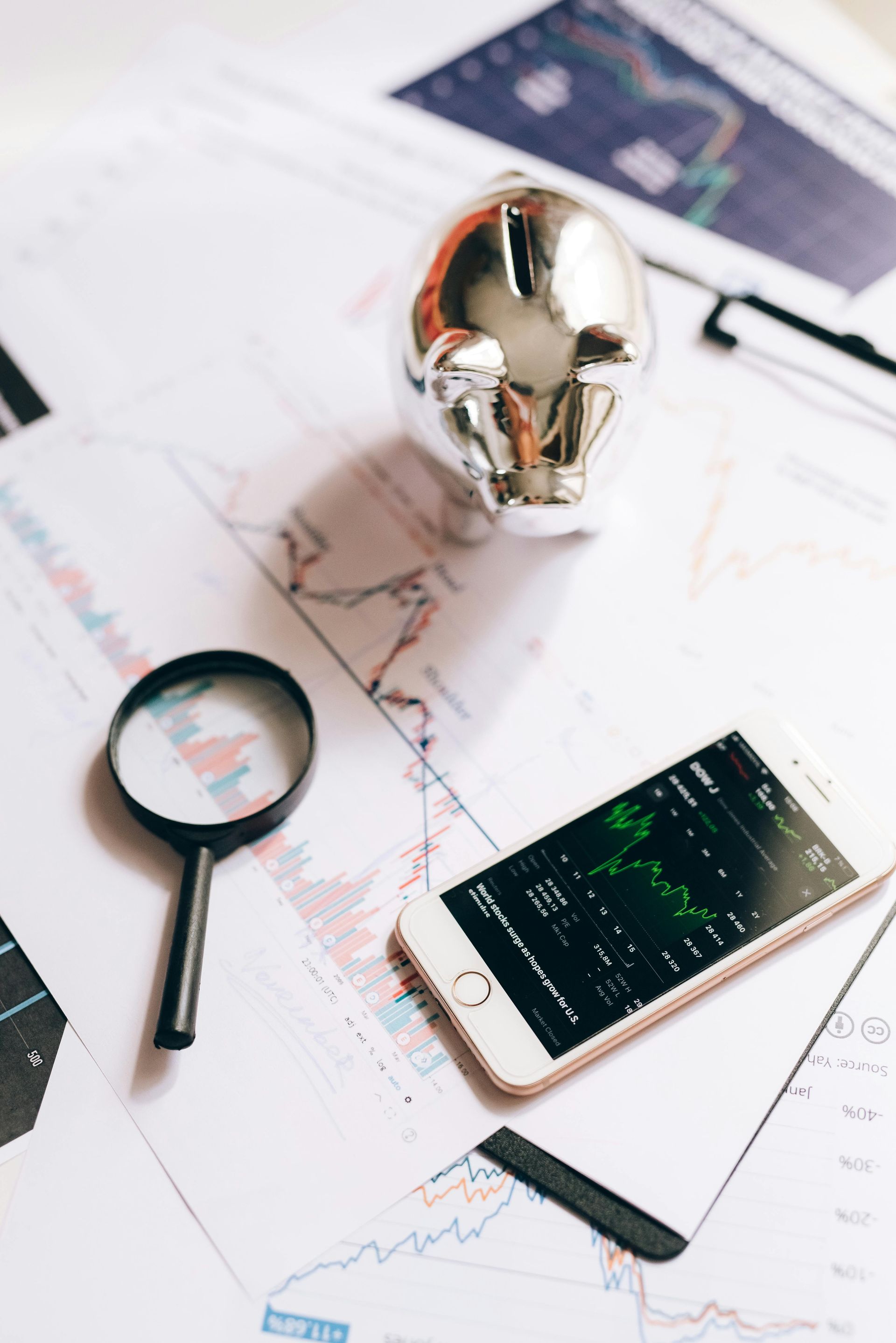 Hay una lupa sobre una mesa al lado de un teléfono celular y una alcancía.