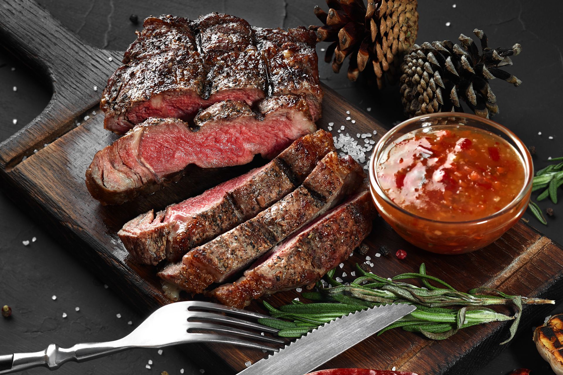 Auf einem Holzschneidebrett liegt ein Steak neben einer Schüssel mit Soße.
