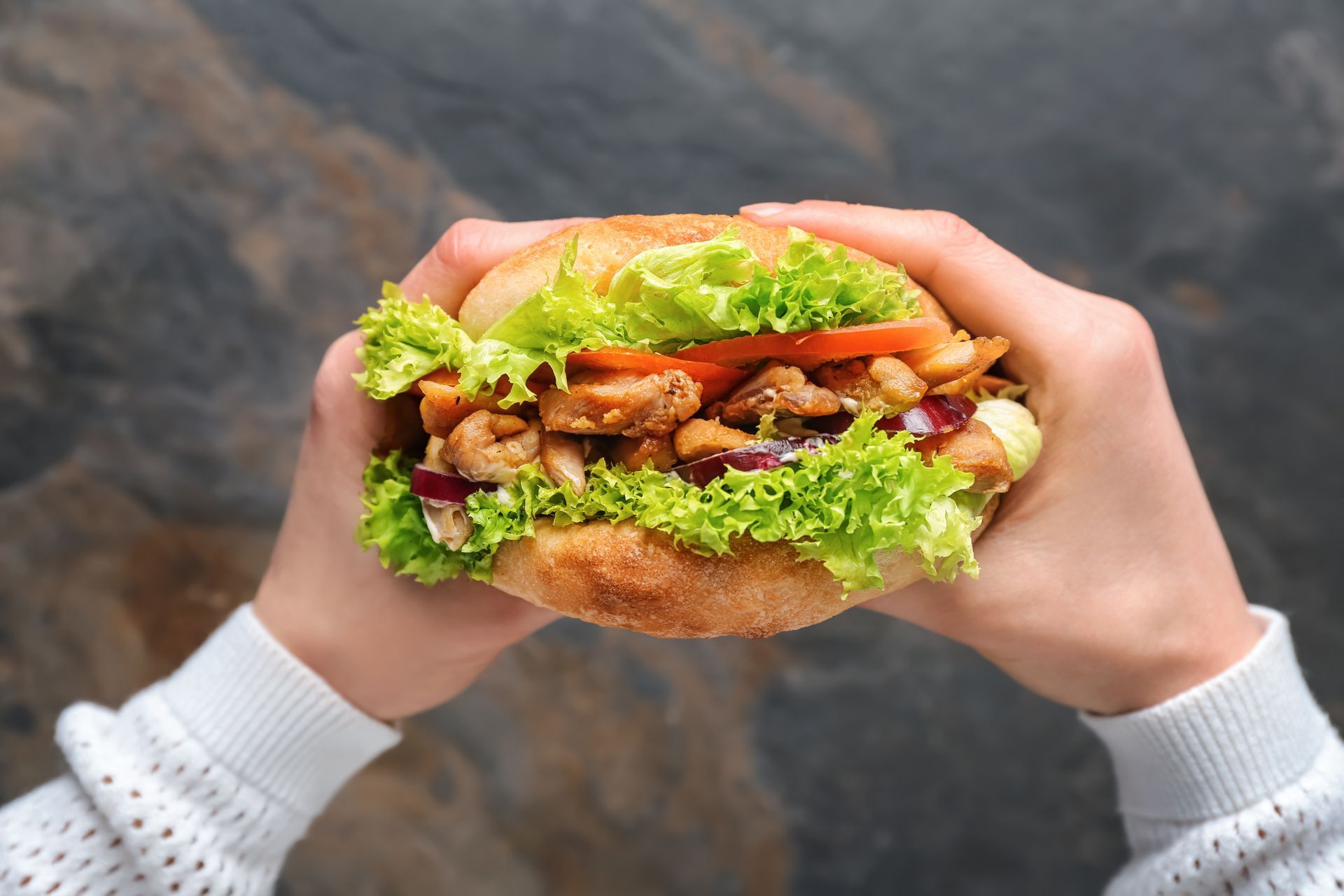 Eine Person hält ein Hühnchensandwich in den Händen.