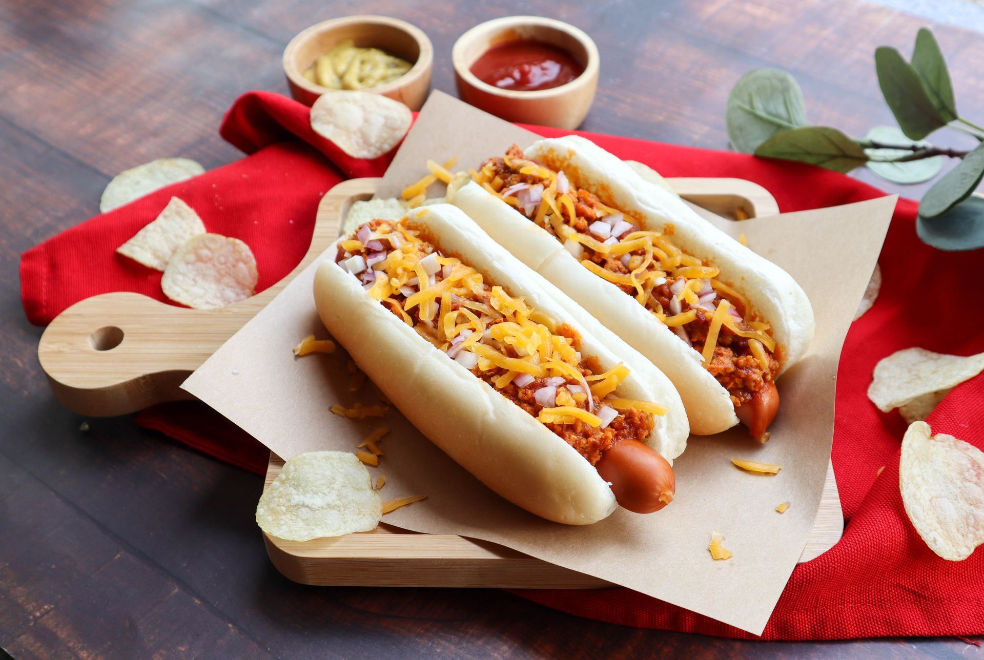 Zwei Hotdogs mit Chili und Käse auf einem Holzschneidebrett.