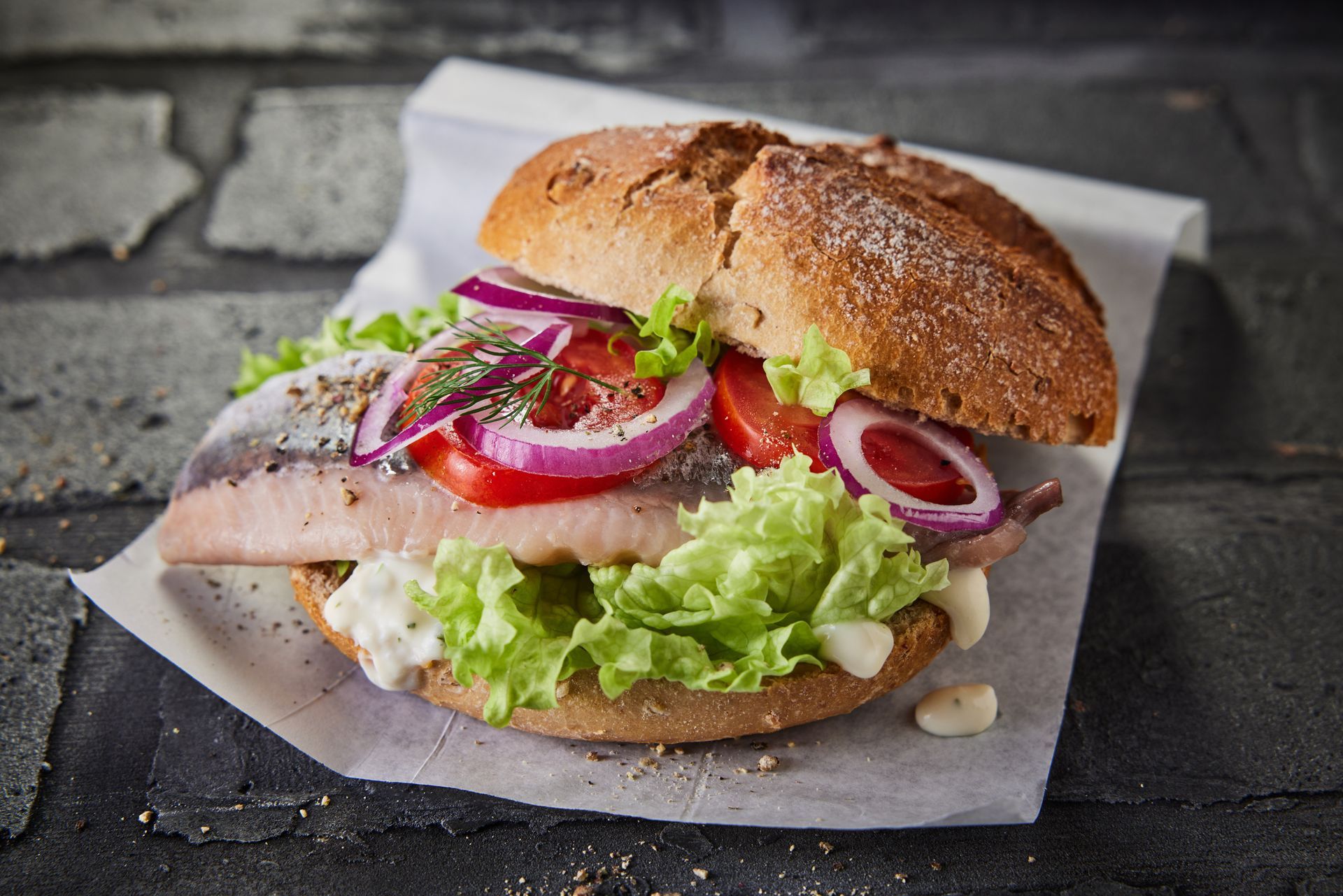 Ein Sandwich mit Salat, Tomaten und Zwiebeln auf einem Brötchen auf einem Stück Papier.