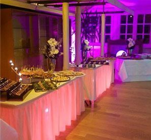 Ein Buffet-Tisch mit violetten Lichtern und Blumen darauf in einem Raum.