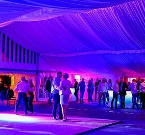Eine Gruppe von Menschen tanzt in einem Zelt mit violetten Lichtern.
