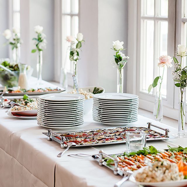 Ein Buffet-Tisch mit Tellern, Besteck und Blumen darauf.