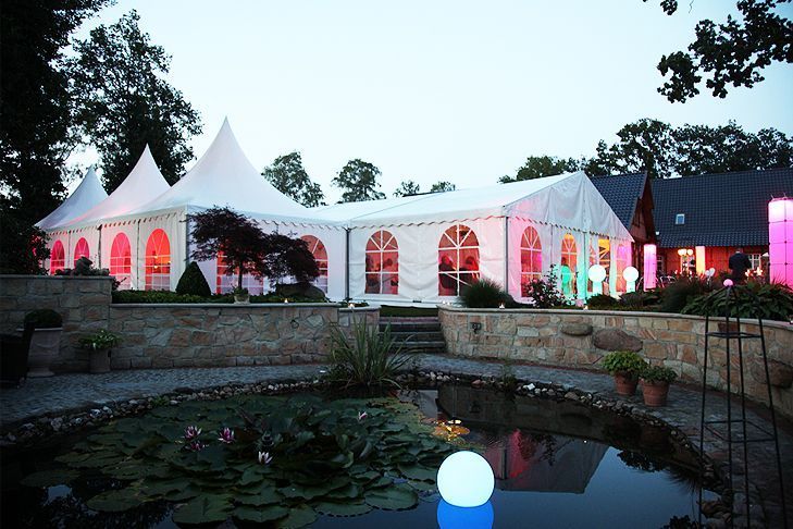 Ein großes weißes Zelt ist vor einem Teich beleuchtet