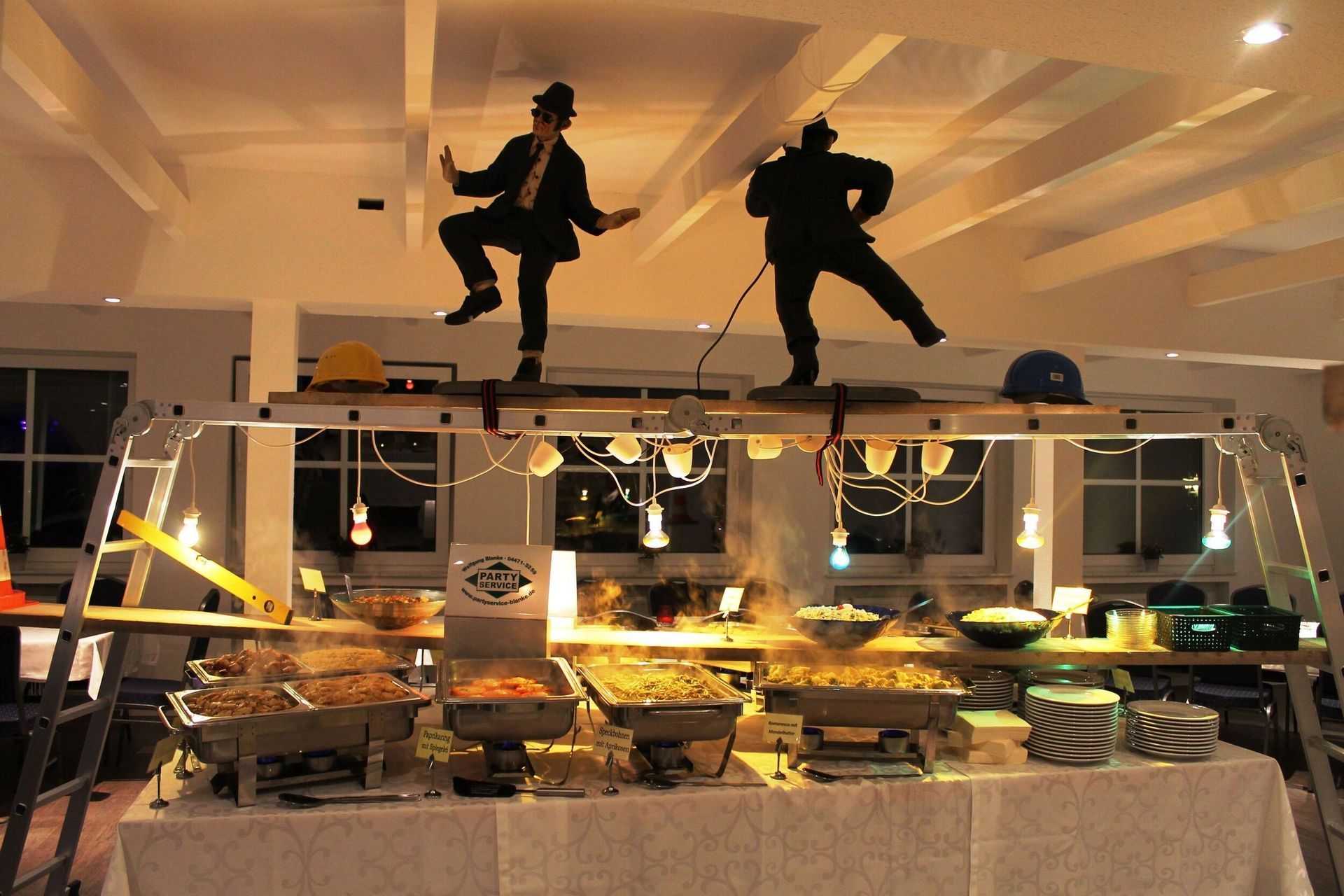 Zwei Männer stehen auf einer Leiter über einem Buffet-Tisch