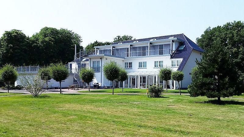 Ein großes weißes Gebäude mit blauem Dach ist von Bäumen und Gras umgeben.