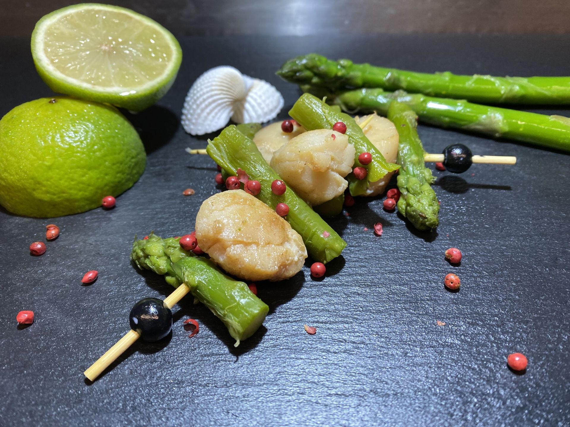 Ein Teller mit Essen mit Spargel und Jakobsmuscheln am Spieß